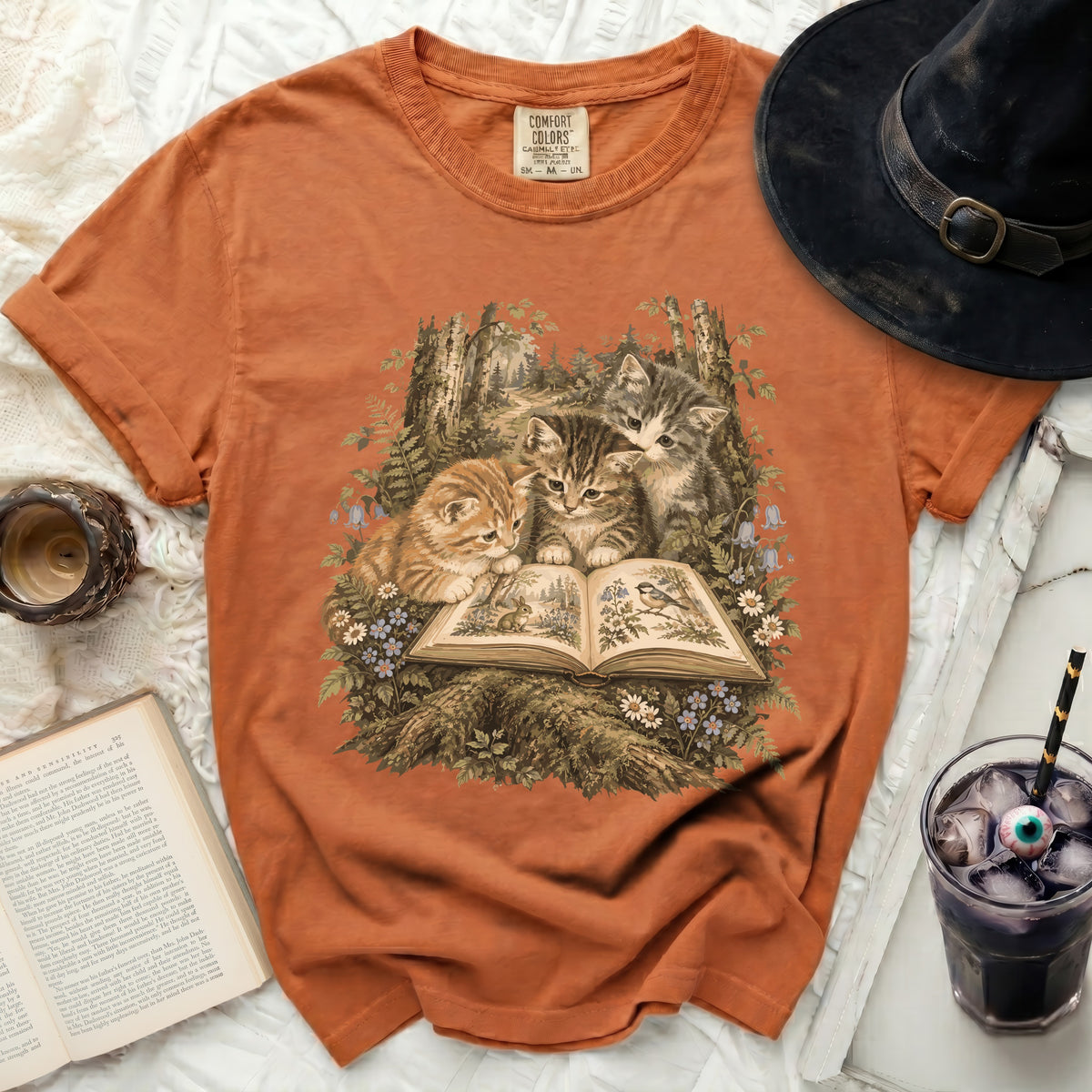 Orange t-shirt with three kittens reading an open book in a forest scene.