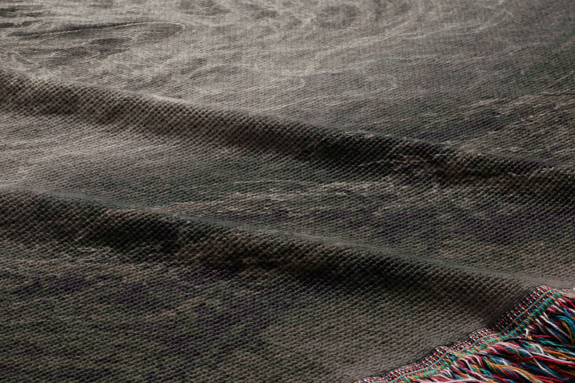 a close-up view of a textured fabric, possibly a blanket or rug, with a dark gray or black color and a slightly curled or folded appearance.