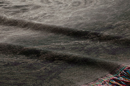 a close-up view of a textured fabric, possibly a blanket or rug, with a dark gray or black color and a slightly curled or folded appearance.
