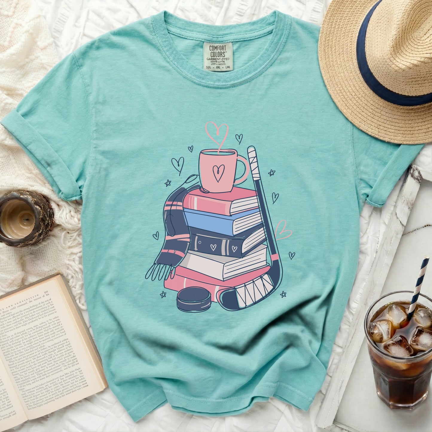 Teal t-shirt with books, hockey stick, mug, and hearts graphic.