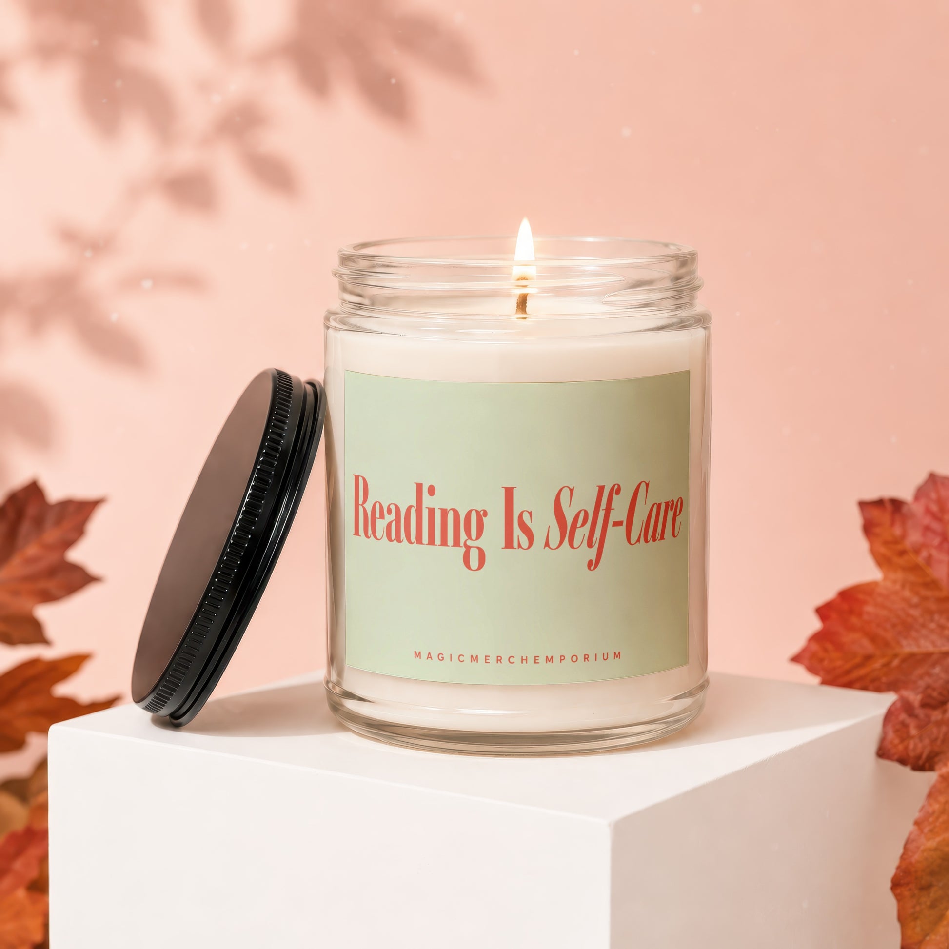 Lit candle with "Reading Is Self-Care" text, lid off, on a white cube.