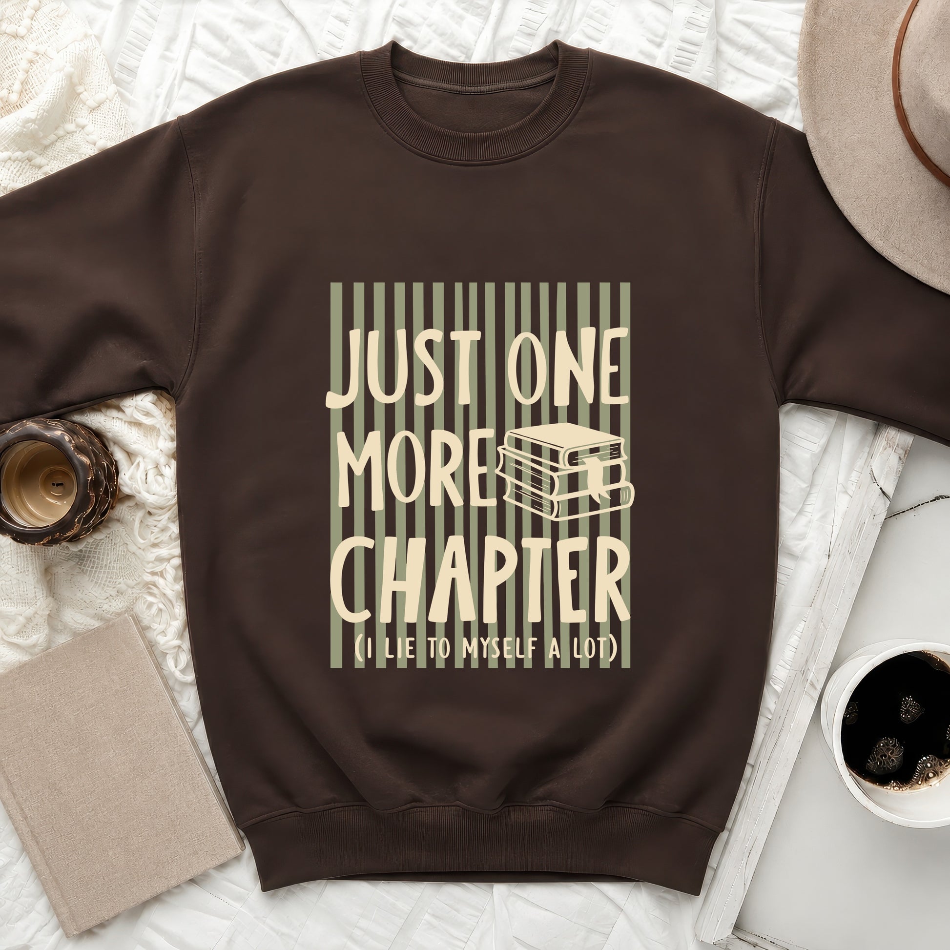 Brown sweatshirt with "Just One More Chapter" and books design.