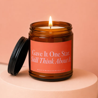 Amber jar candle with lit wick and a label reading "Gave It One Star. Still Think About It."