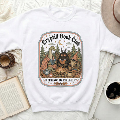 Cryptid Book Club illustration with creatures reading by firelight, text "Meetings by Firelight" below.