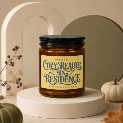 Amber candle with black lid labeled "Official Cozy Reader In Residence".