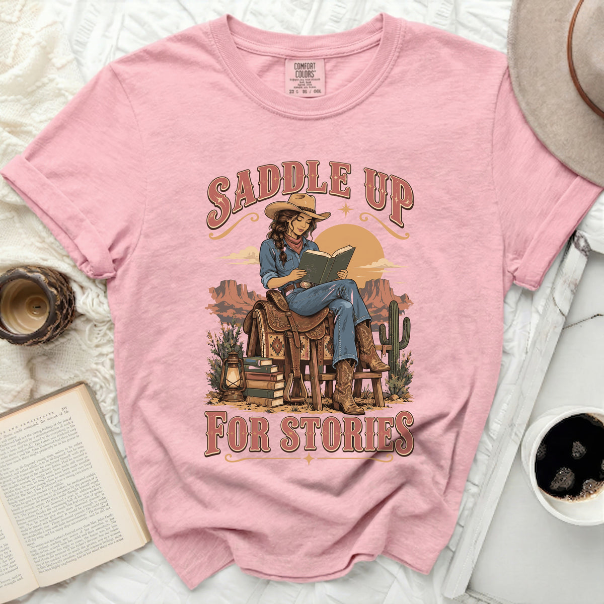 Pink t-shirt with "Saddle Up For Stories" text and cowgirl reading book graphic.