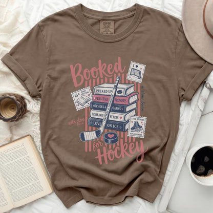 Brown t-shirt with "Booked for Hockey" text and book-themed icons.