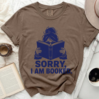 T-shirt with blue graphic of a woman reading and text "SORRY, I AM BOOKED."