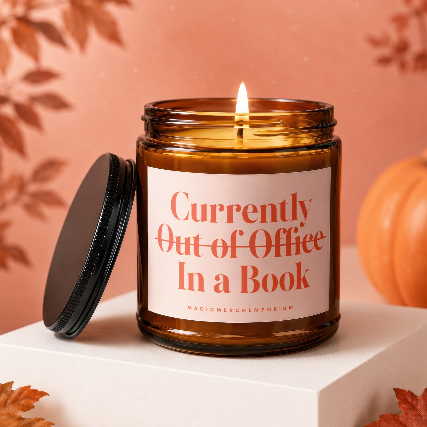 Amber candle with lit wick, lid off, reading "Currently Out of Office In a Book."
