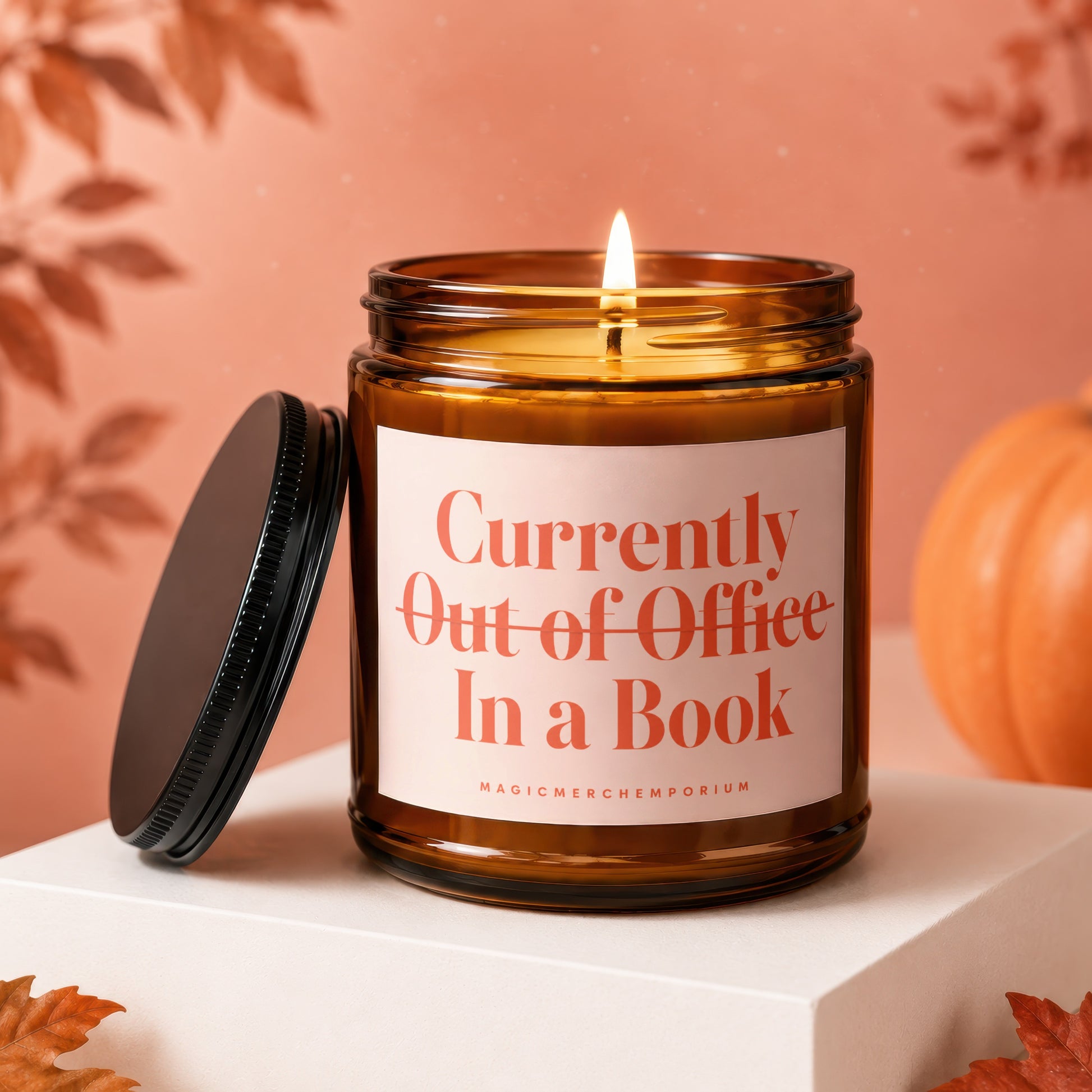 Amber candle with lit wick, lid off, reading "Currently Out of Office In a Book."