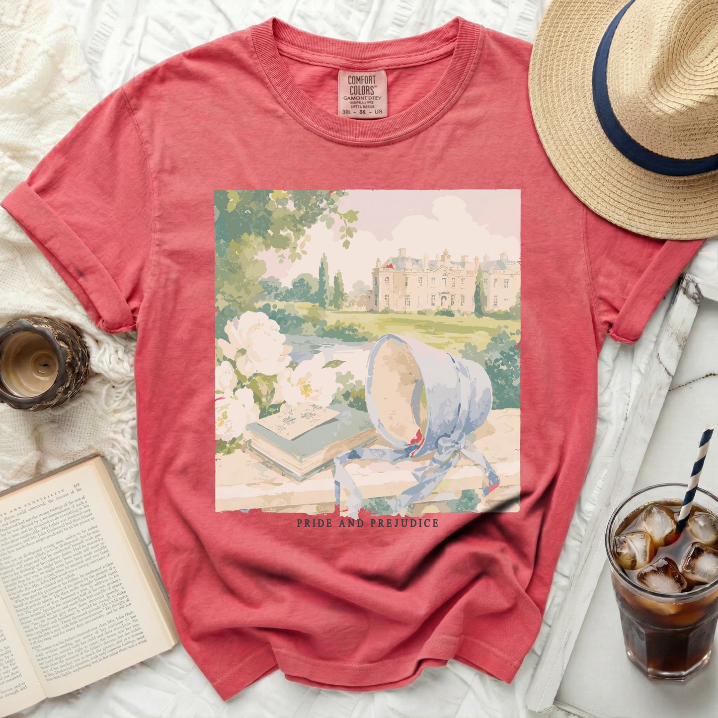 Coral t-shirt with Pride and Prejudice graphic of a manor and books.