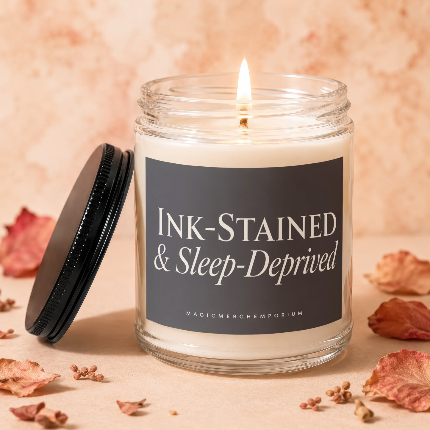 Lit candle in glass jar labeled "INK-STAINED & Sleep-Deprived" with lid off.