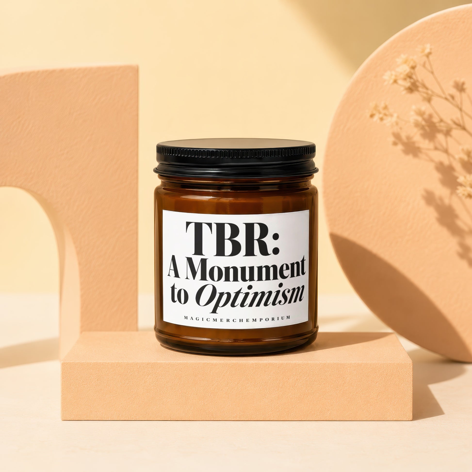 Candle with white label reading "TBR: A Monument to Optimism" by MagicMerch Emporium.