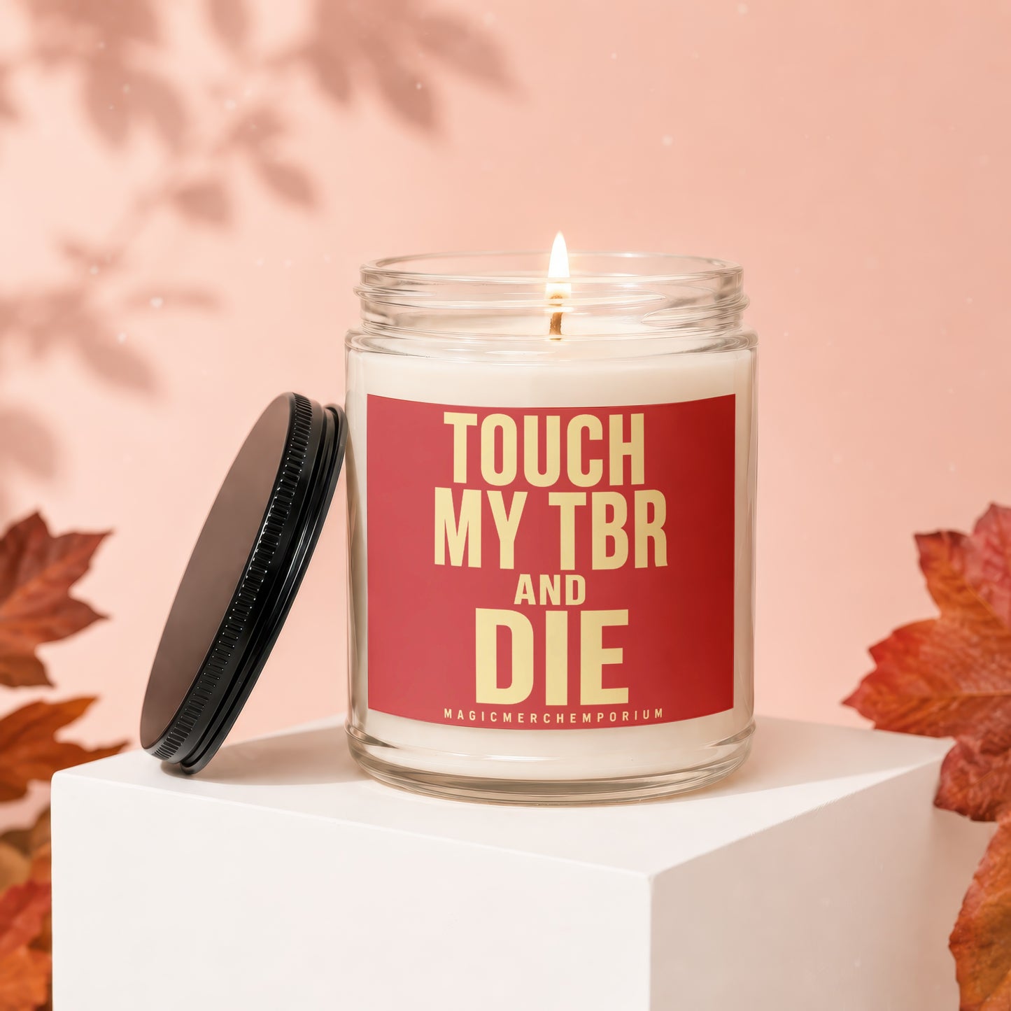Lit candle in glass jar with red label reading "TOUCH MY TBR AND DIE".
