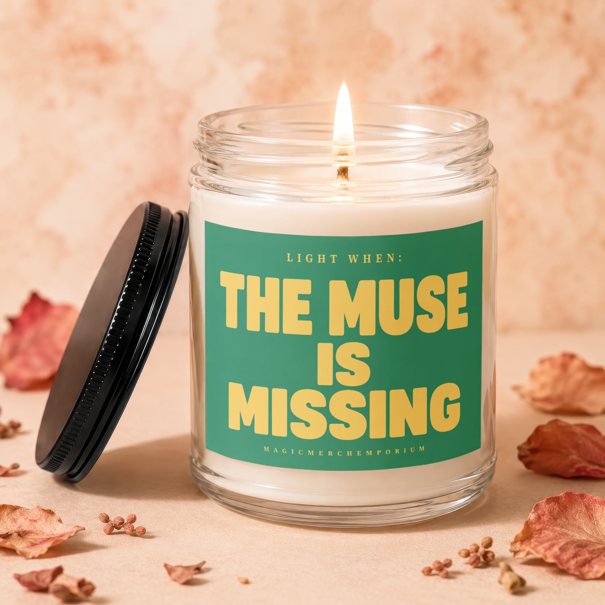 Glass candle labeled "LIGHT WHEN: THE MUSE IS MISSING" with lit wick.
