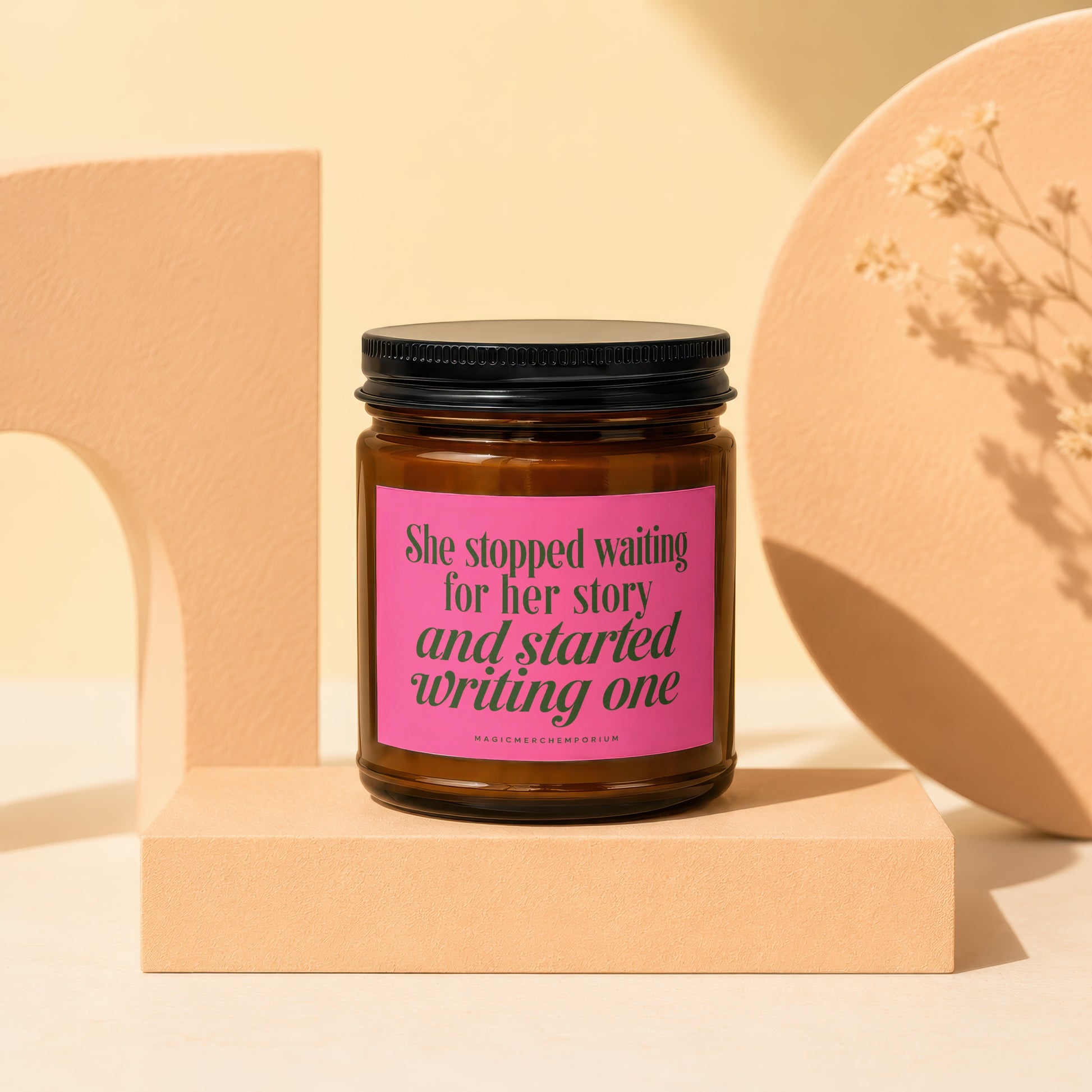 Brown glass candle with pink label reading "She stopped waiting for her story and started writing one."