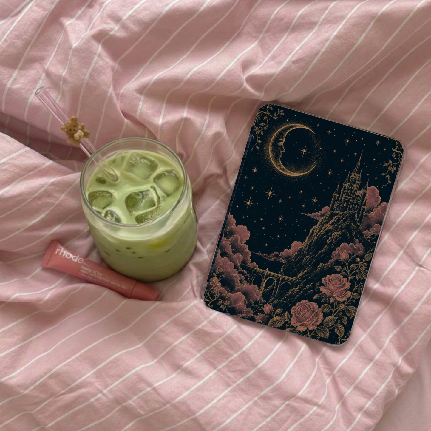 Aesthetic book cover with castle, moon, and roses, next to a green drink and lip balm.