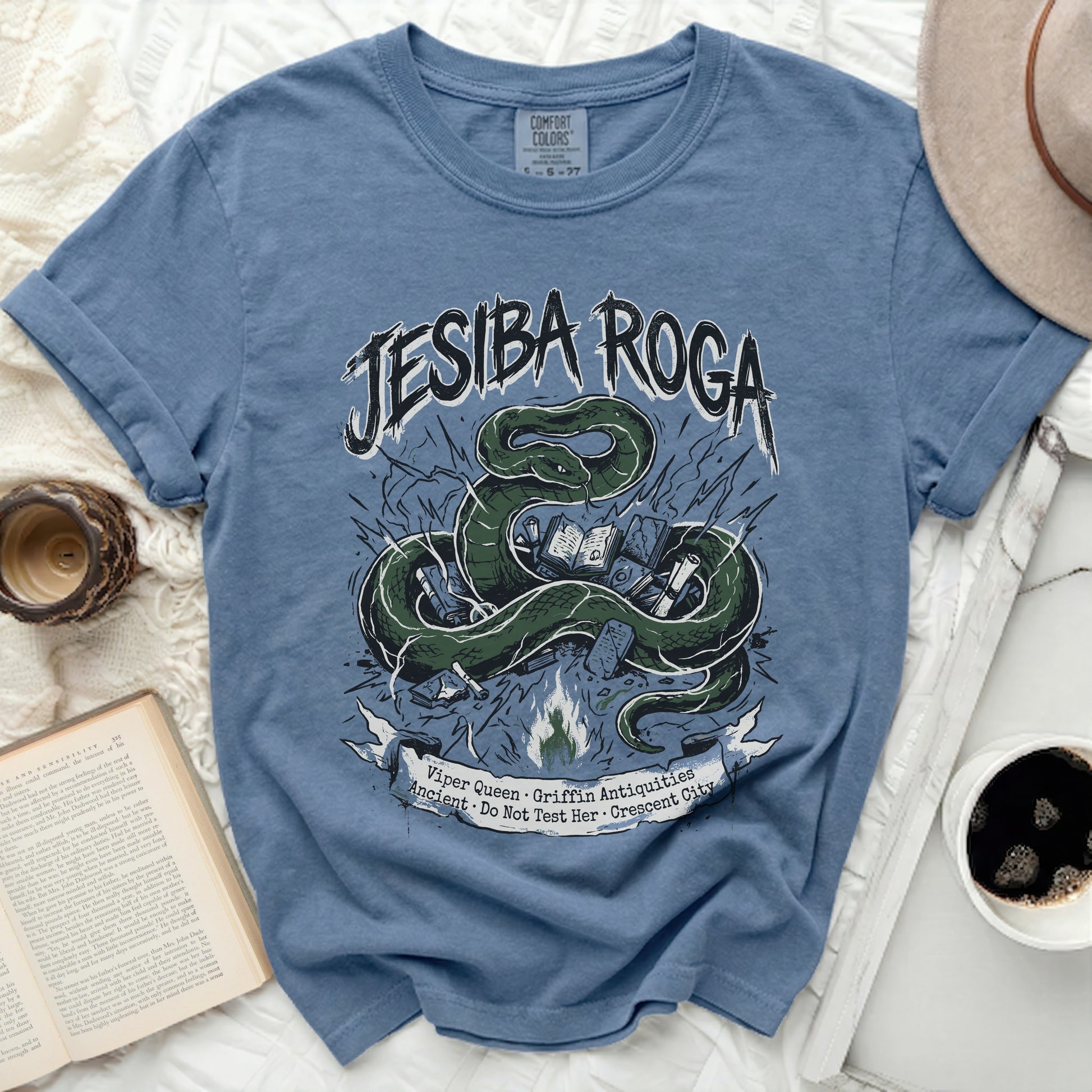 Blue t-shirt with green snake and book graphic, "Jesiba Roga" text.