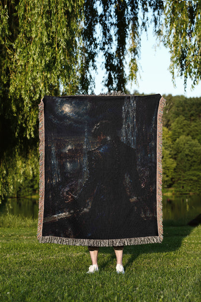 A person stands in a grassy field, holding a large square blanket with a painting of a person on it.