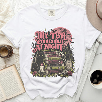 White t-shirt with "My TBR Comes Out At Night" text and spooky illustration.