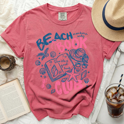 Pink t-shirt with "Beach Book Club" graphic and seashells.