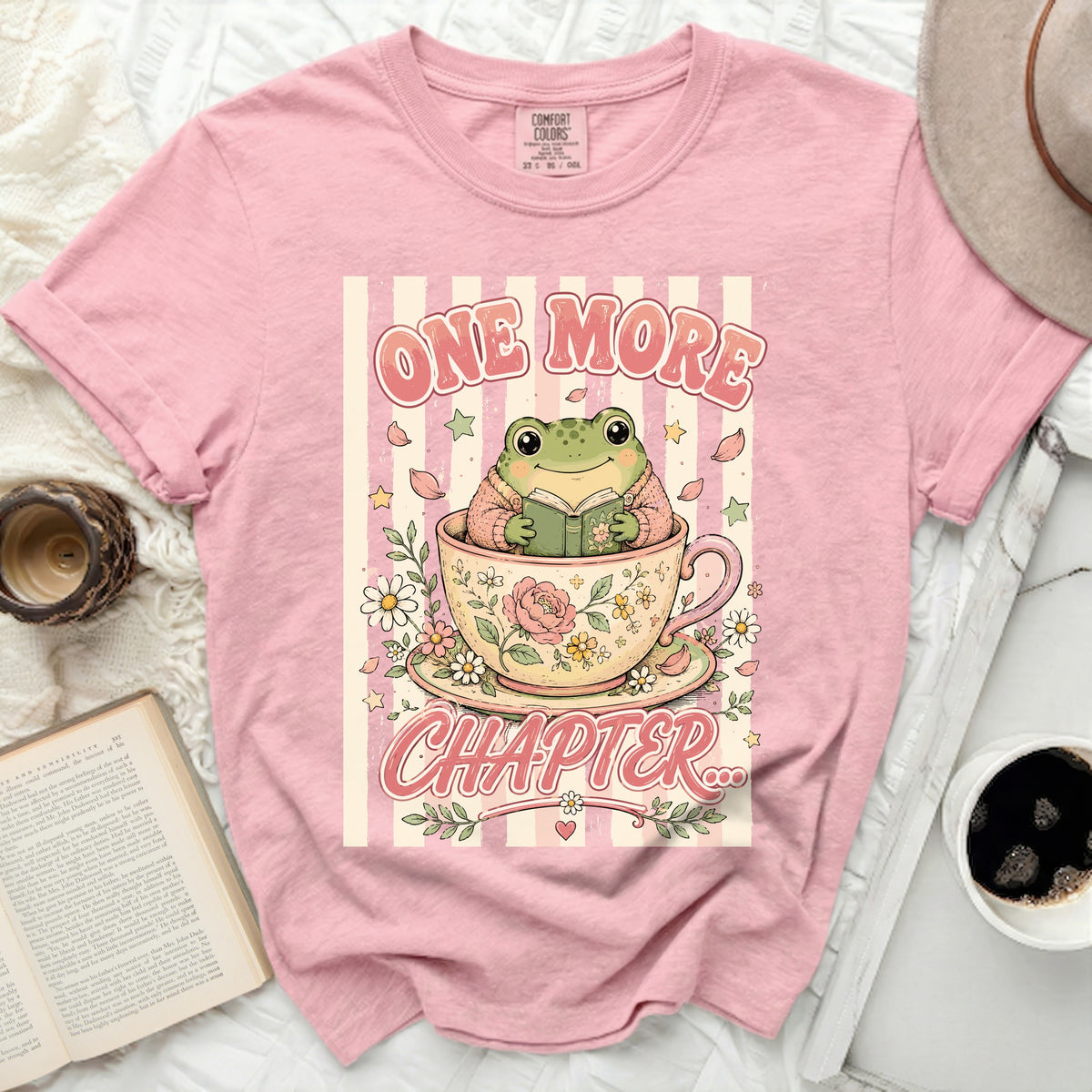 Pink t-shirt with a frog reading a book inside a teacup.