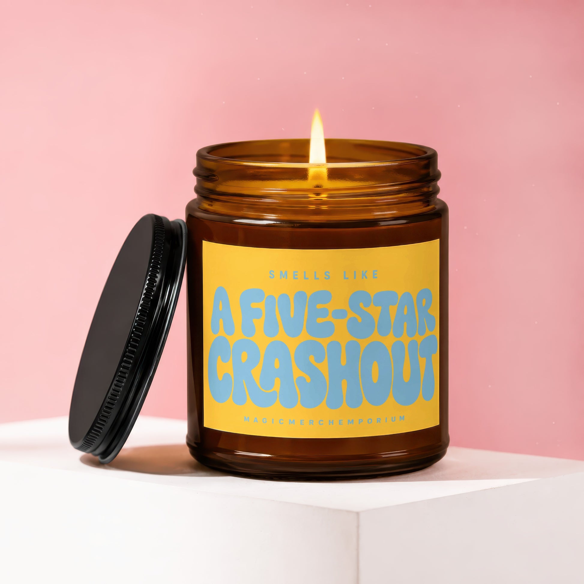 Amber glass candle with lit flame and black lid asks "Smells Like A Five-Star Crashout".