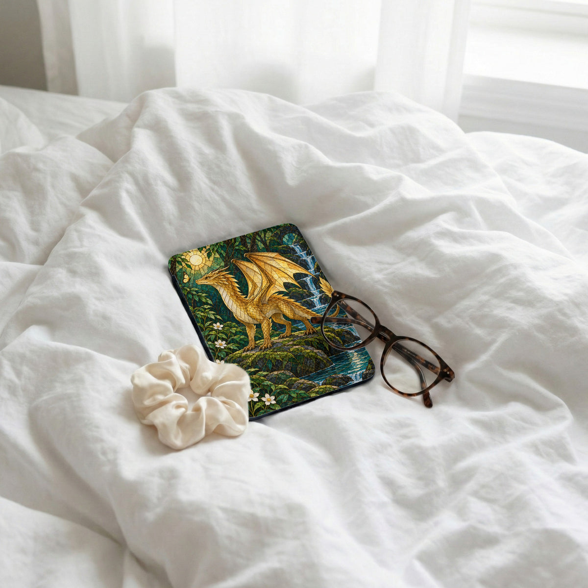 Case with golden dragon and waterfall art, scrunchie, and glasses on white sheets.