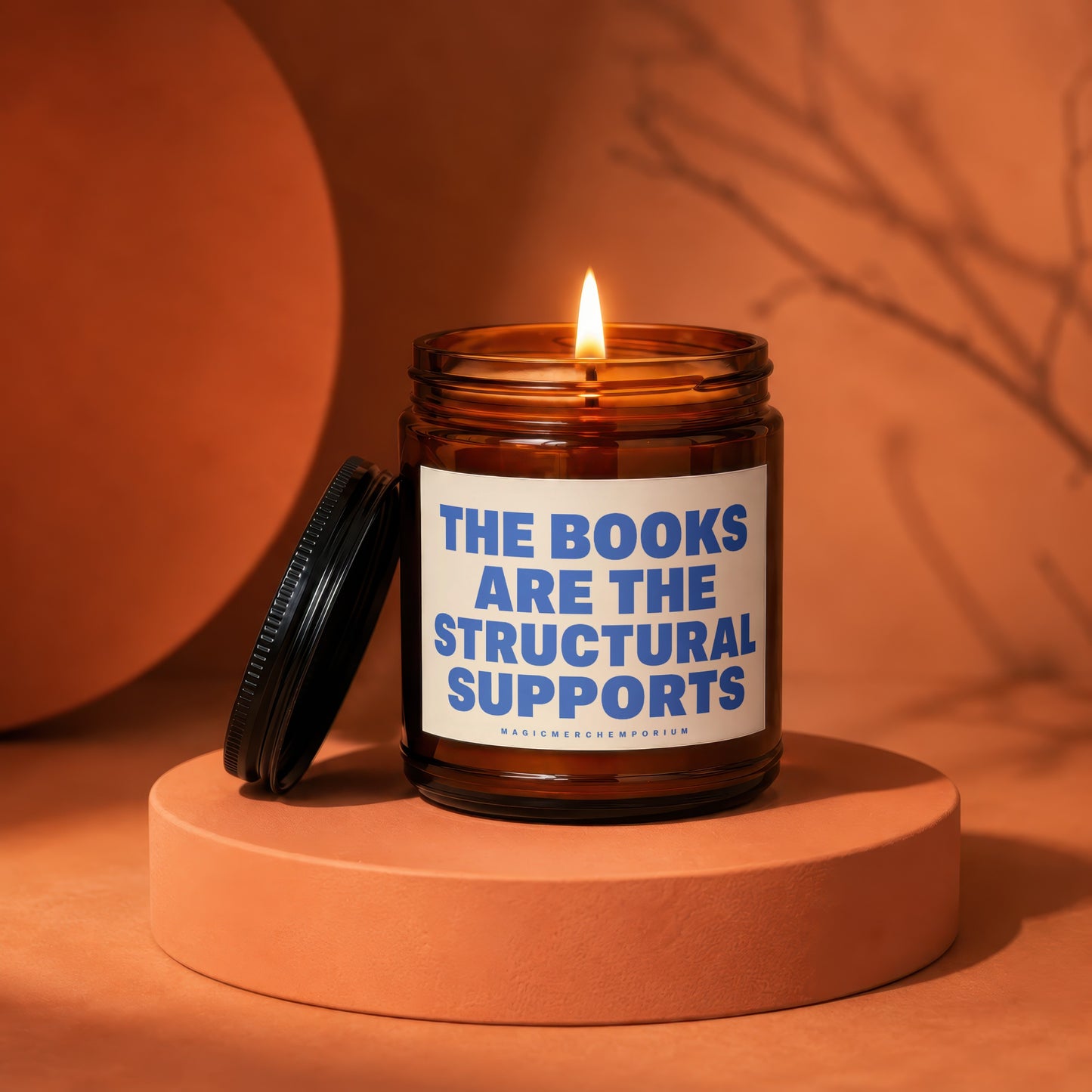 Amber jar candle with lit flame and label reading "The Books Are The Structural Supports".