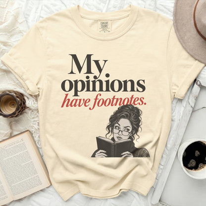 Cream t-shirt with graphic "My opinions have footnotes" and illustration of woman reading.