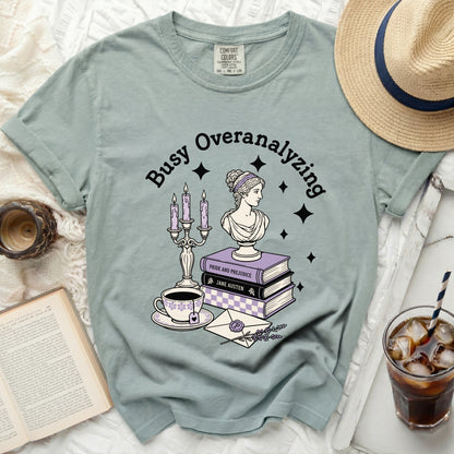 Green t-shirt with "Busy Overanalyzing" text and bookish illustration.