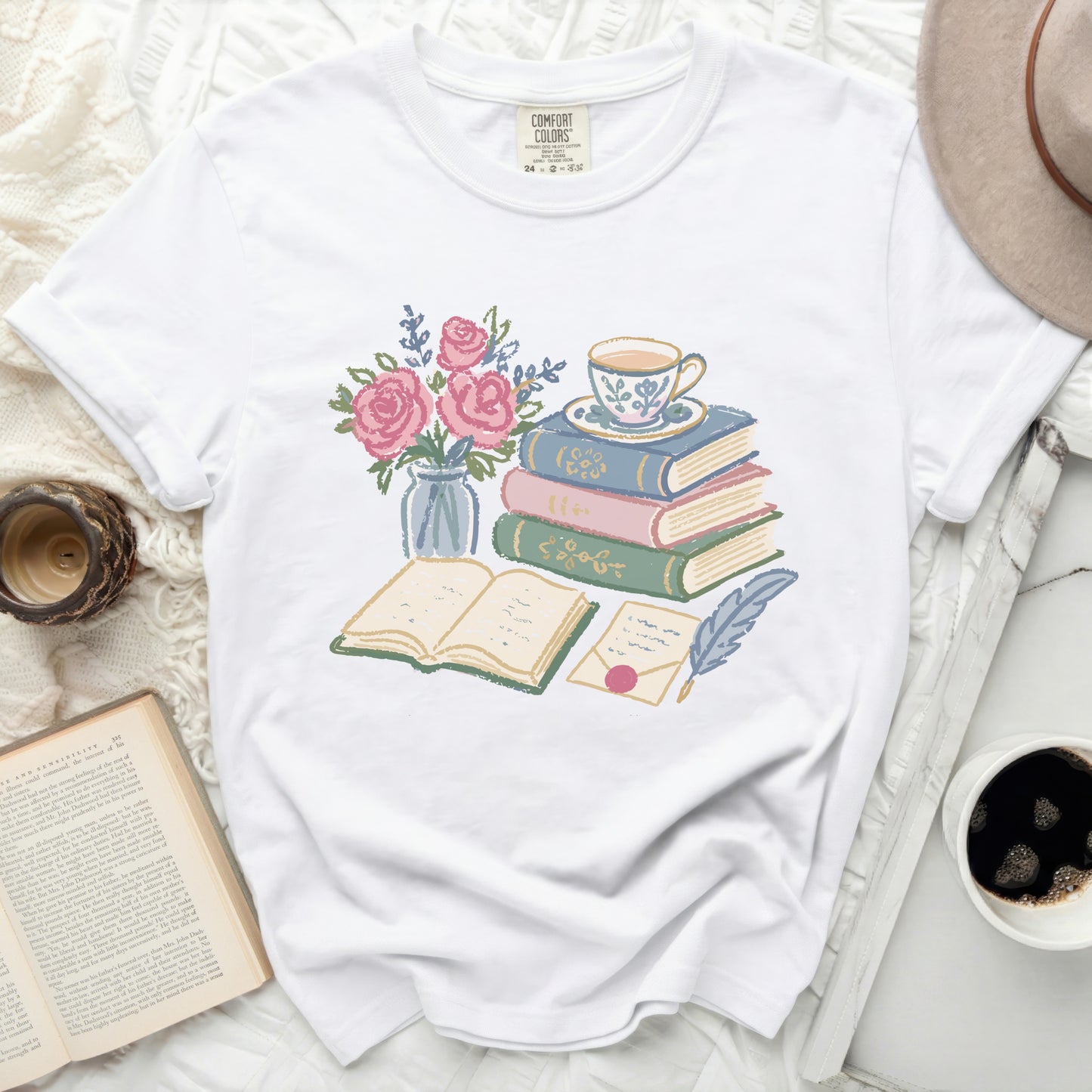 White t-shirt with a stack of colorful books, teacup, envelope, quill, and roses.