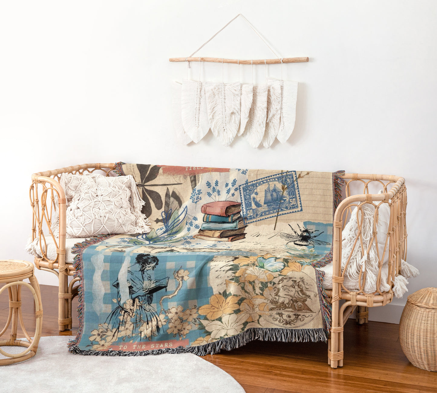 a cozy living room with a wicker sofa adorned with a colorful throw blanket that has a floral and bird motif. The blanket is draped over the sofa, creating a warm and inviting atmosphere. Above the sofa, there is a hanging decoration made of white feathers, adding a touch of elegance to the room. The room also includes a small table and a woven basket, contributing to the overall rustic and charming aesthetic.