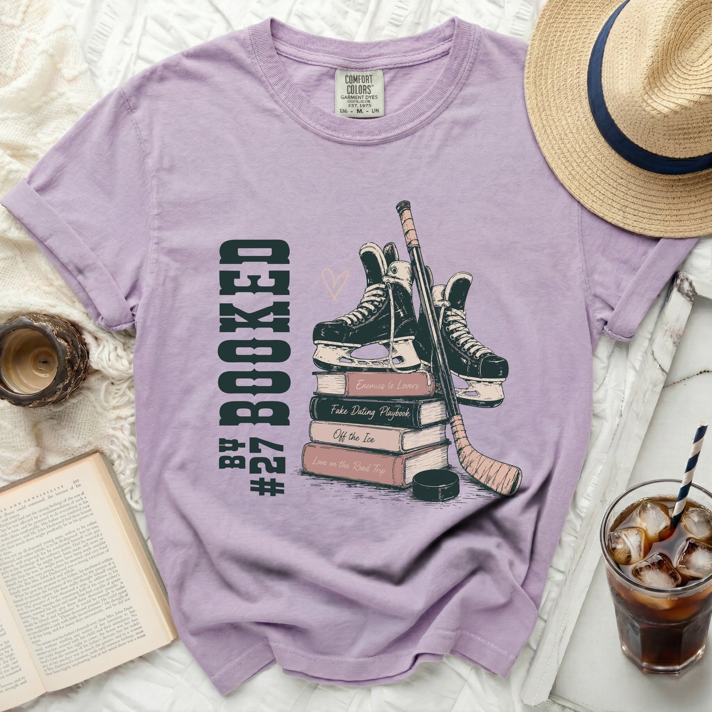 Lavender graphic tee with hockey skates, stick, and books, "Booked" text.
