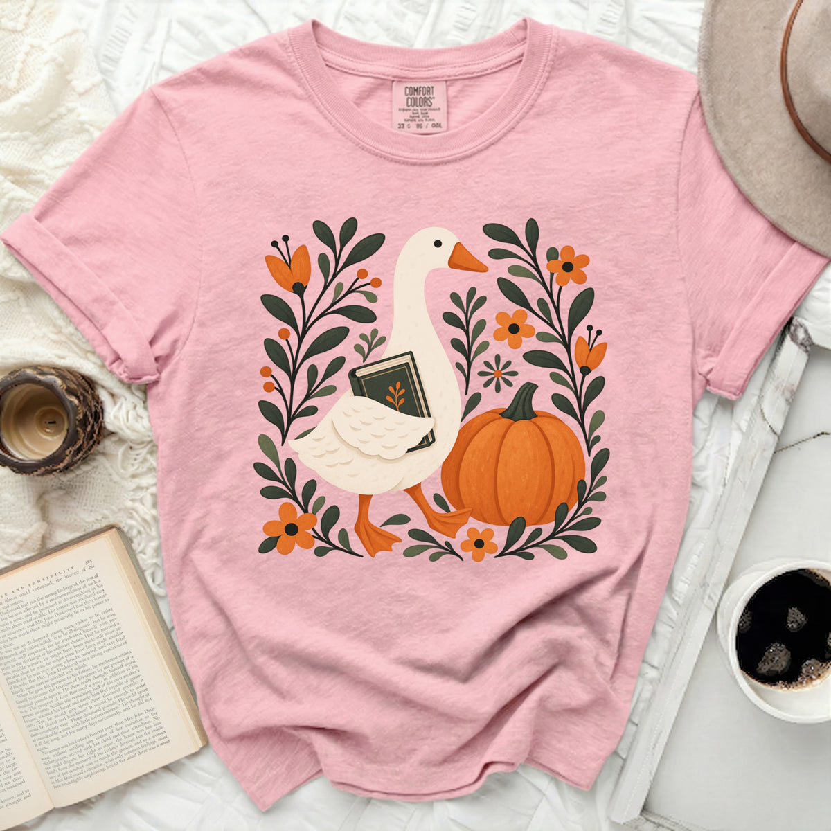 Pink t-shirt with a white goose holding a book and a pumpkin.