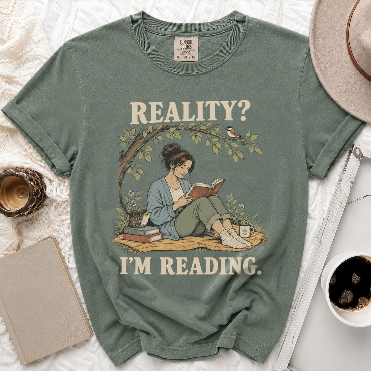 Green t-shirt with "Reality? I'm Reading" and a woman reading under a tree.