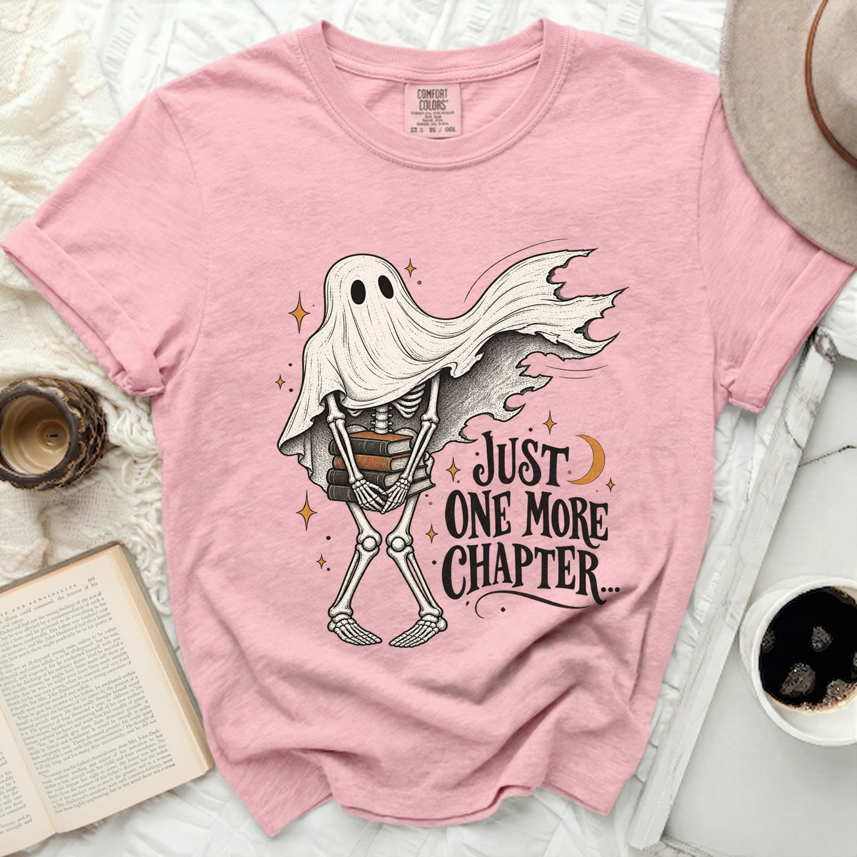 Pink t-shirt with skeleton ghost holding books and text "Just One More Chapter".