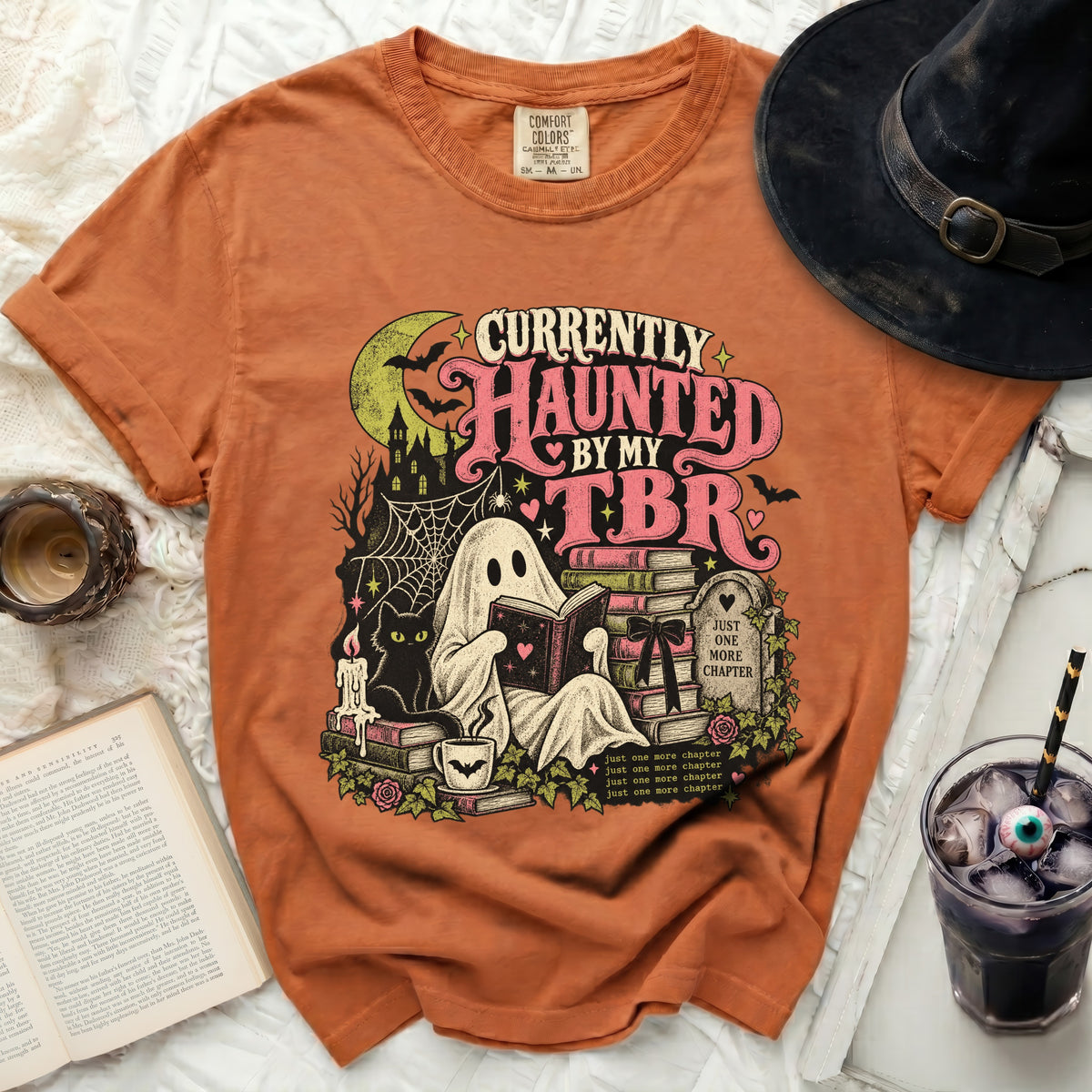 Orange t-shirt with ghost reading among books and Halloween imagery.