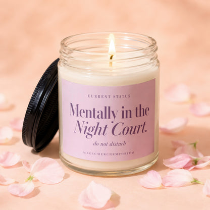 A lit soy candle in a glass jar featuring a pink label with purple text.