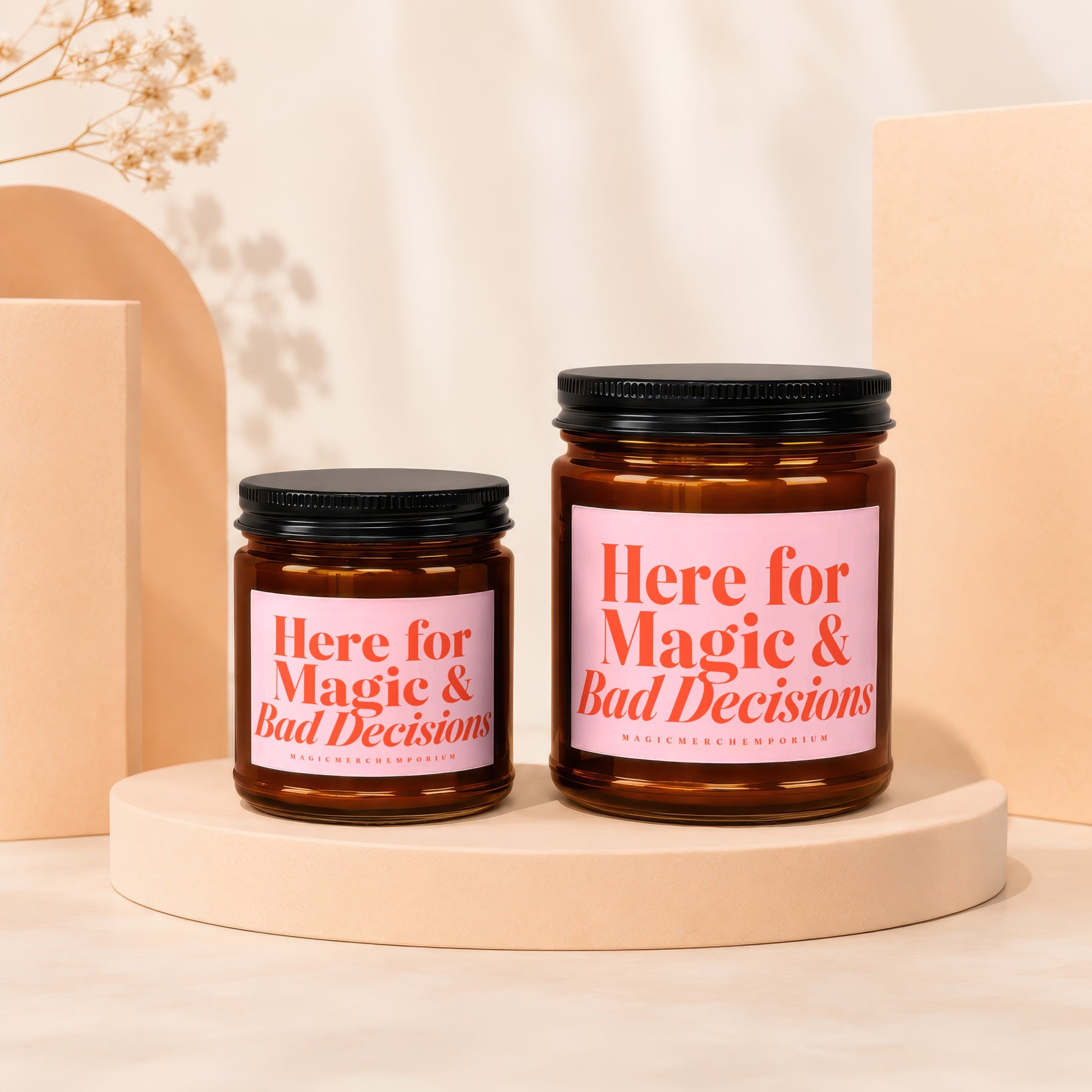 Two amber glass candles with pink labels reading "Here for Magic & Bad Decisions."
