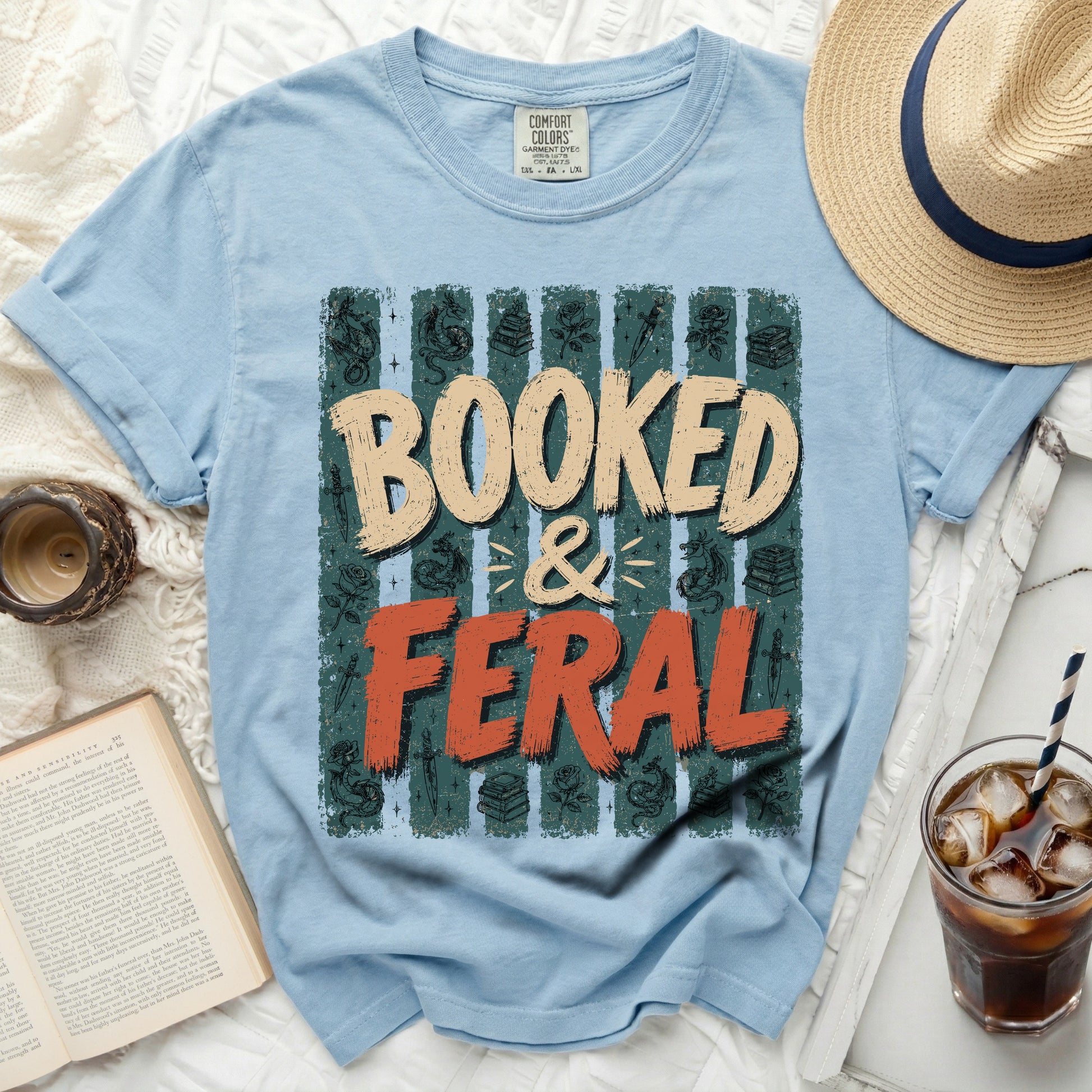 Light blue t-shirt with "BOOKED & FERAL" graphic and book illustrations.
