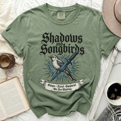 Olive green t-shirt with "Shadows and Songbirds" and a bird with a sword.
