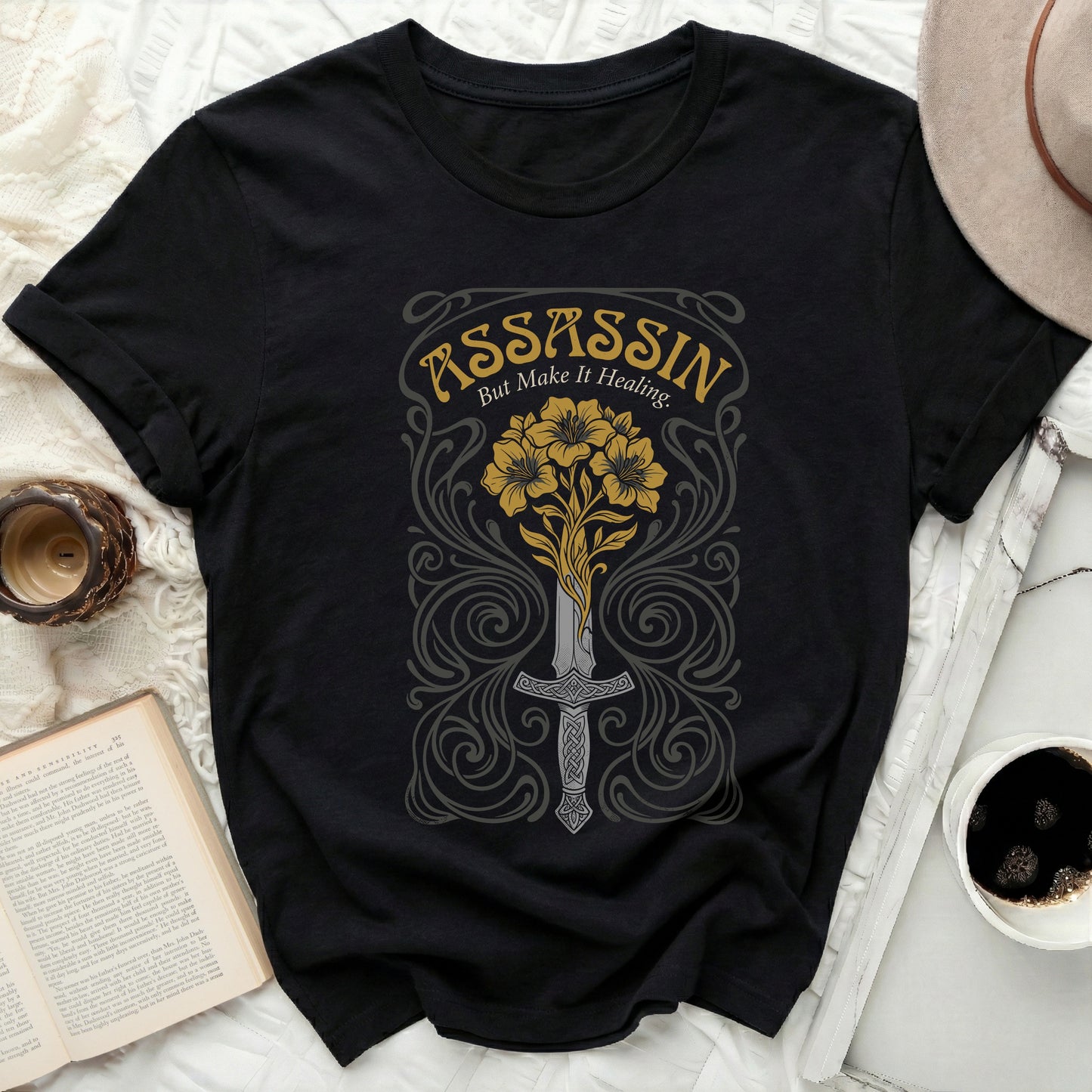 Black t-shirt with "Assassin but Make It Healing" floral and sword graphic.