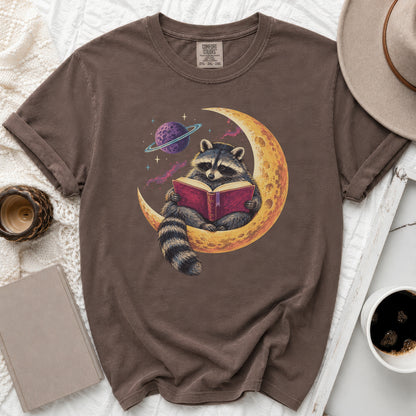Brown t-shirt with graphic of raccoon reading a book on the moon with a planet.