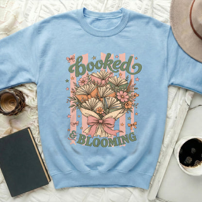 Light blue sweatshirt with "Booked & Blooming" text and book bouquet design.