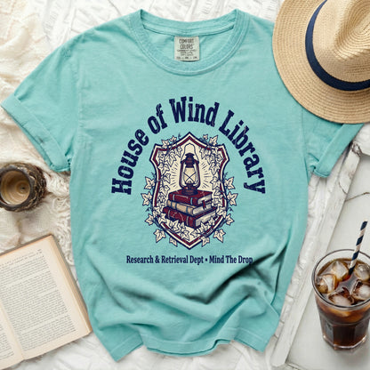 Teal t-shirt with "House of Wind Library" crest graphic and text.