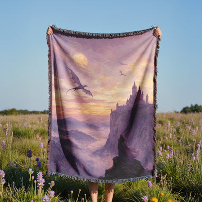 A person is holding a large blanket with a dragon and castle scene printed on it, standing in a field with purple flowers.
