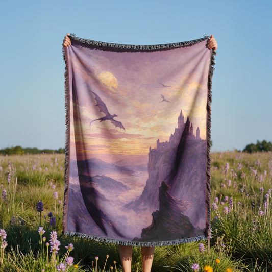 A person is holding a large blanket with a dragon and castle scene printed on it, standing in a field with purple flowers.