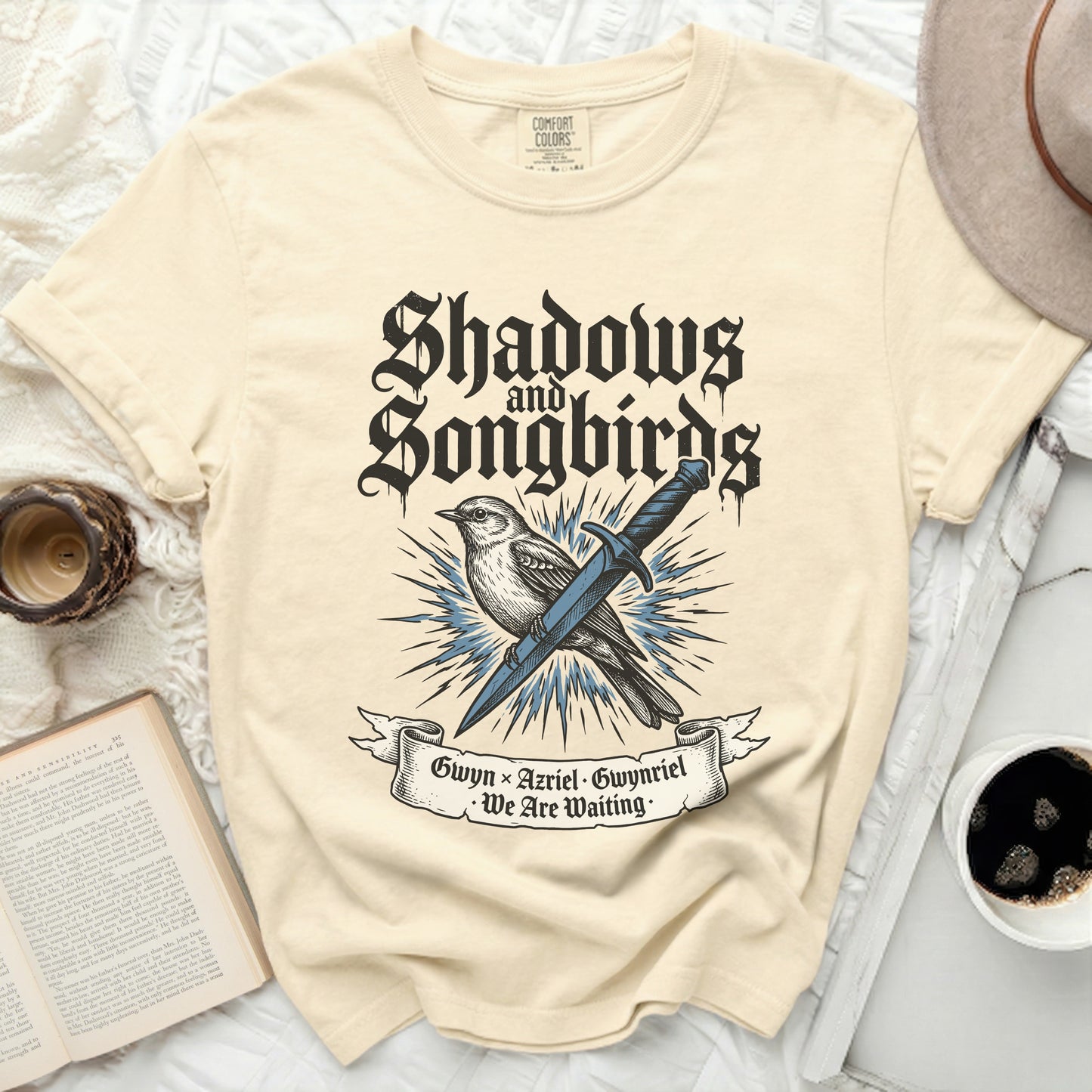 Cream t-shirt with "Shadows and Songbirds" and sword graphic.