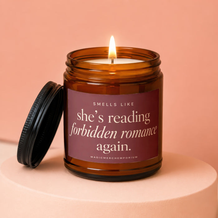 Amber glass candle with lit wick and lid off, labeled "Smells like she's reading forbidden romance again."
